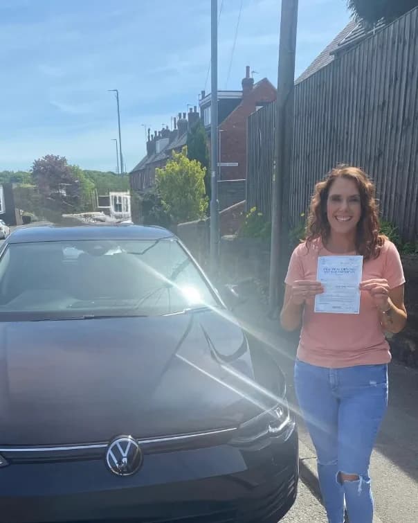 An ACE learner holding her pass certificate beside the school's black VW Golf