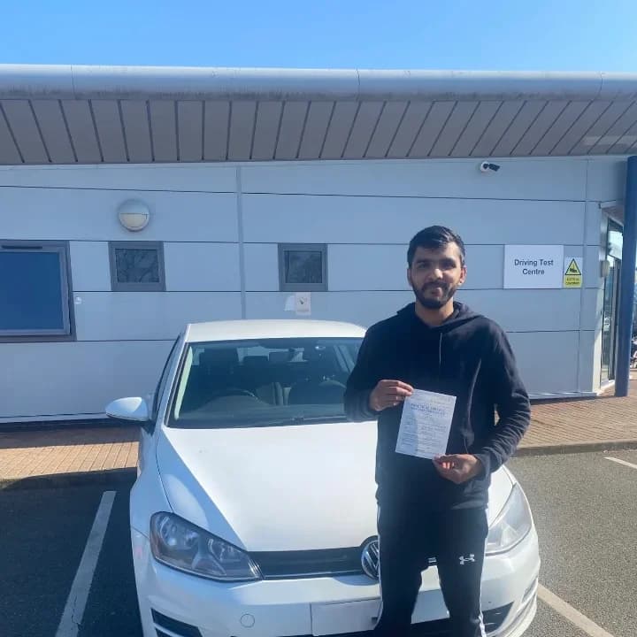 Learner in a black top holding a pass certificate beside a white hatchback