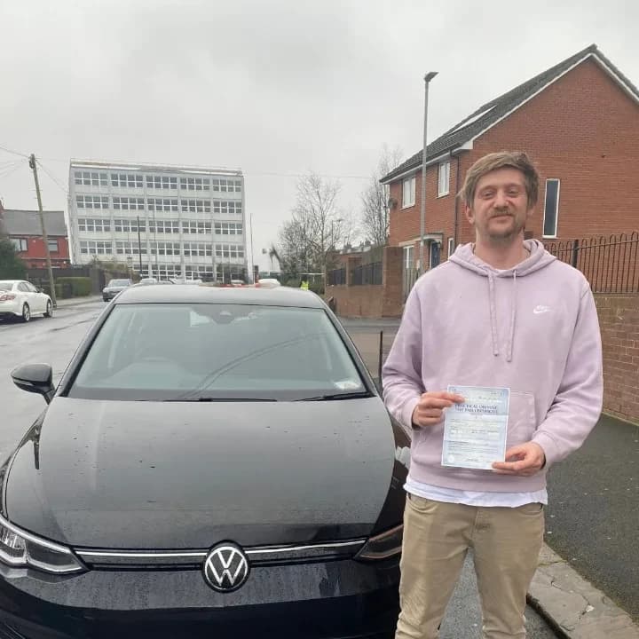 Learner in a lilac hoodie holding a pass certificate beside the black VW Golf