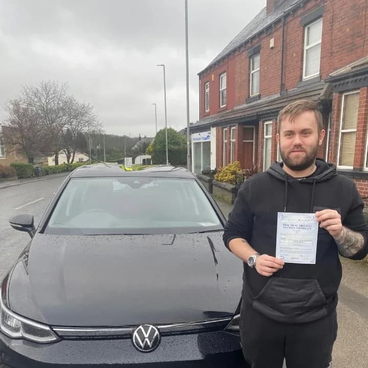 Learner in a black hoodie holding a pass certificate beside the black VW Golf