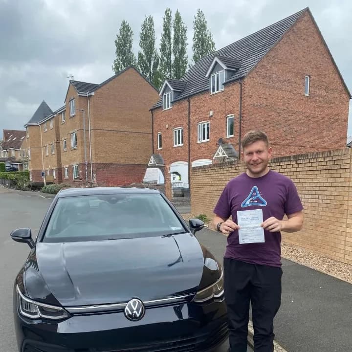 Learner in a purple top holding a pass certificate beside the black VW Golf