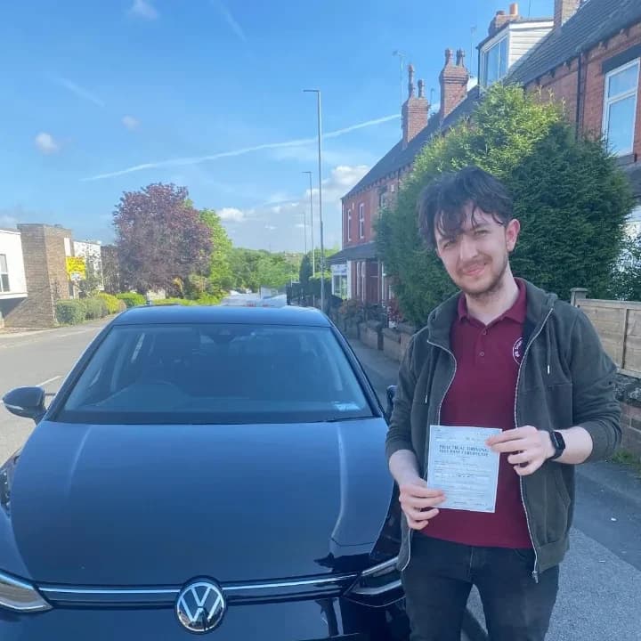 Learner in a black jacket and red shirt holding a pass certificate beside the black VW Golf