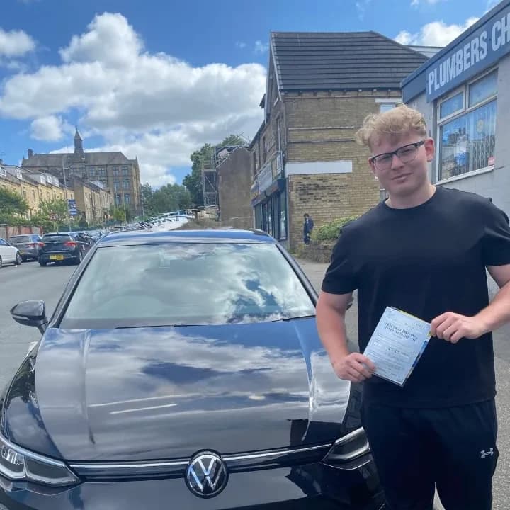 Learner in a black T-shirt holding a pass certificate beside the black VW Golf