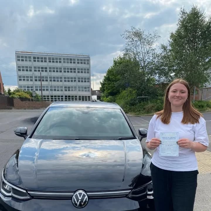 Learner in a white shirt holding a pass certificate beside the black VW Golf